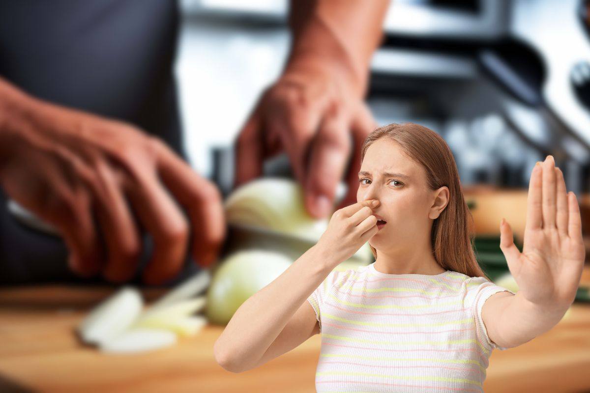 uomo che usa cipolla in cucina e donna che fa stop con le mani e si ottura il naso