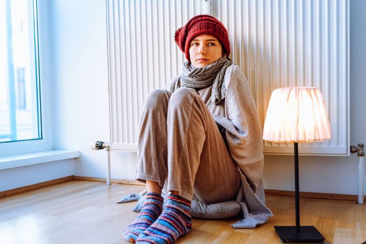 donna con cappello accanto al termosifone