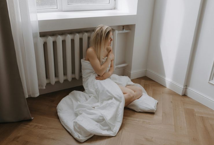 donna avvolta nella coperta accanto al termosifone 