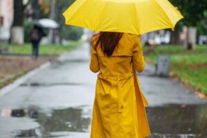 Donna con ombrello e impermeabile giallo in strada dove piove
