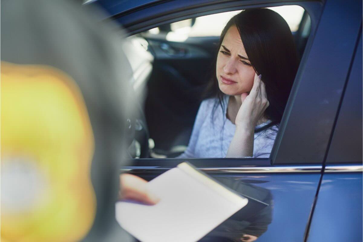 Donna al volante un po' stordita, qualcuno di fronte a lei con un foglio