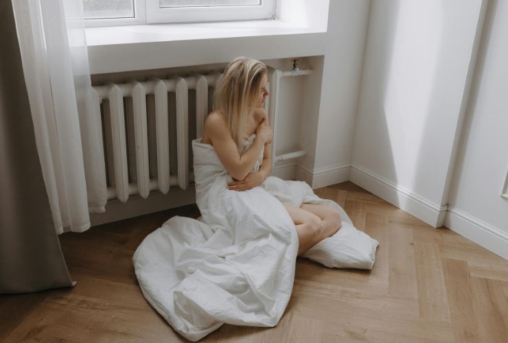 donna avvolta in una coperta accanto al termosifone